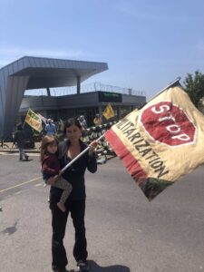 woman holding baby and a flag banner that reads "Stop Militarization"